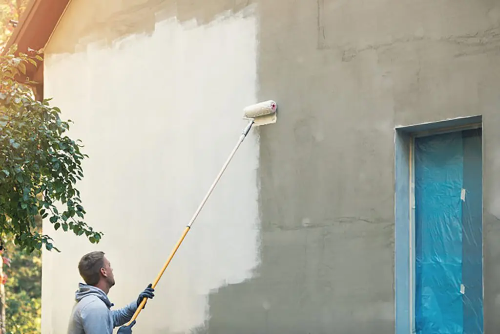 Painter rolling fresh paint onto the exterior wall of a house
