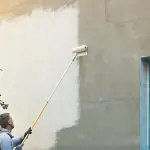 Painter rolling fresh paint onto the exterior wall of a house